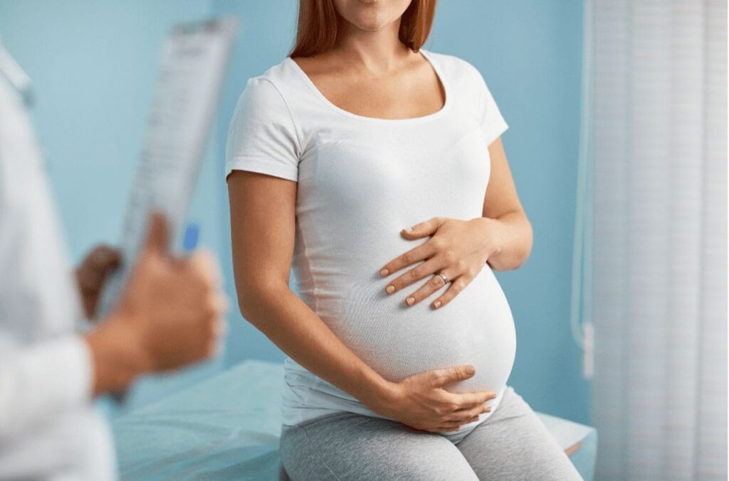 An expecting mother holding her belly at a prenatal chiropractic office.