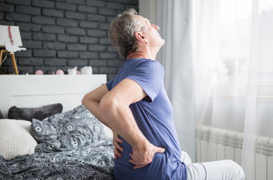 Man waking up with back pain and holding his lower back.