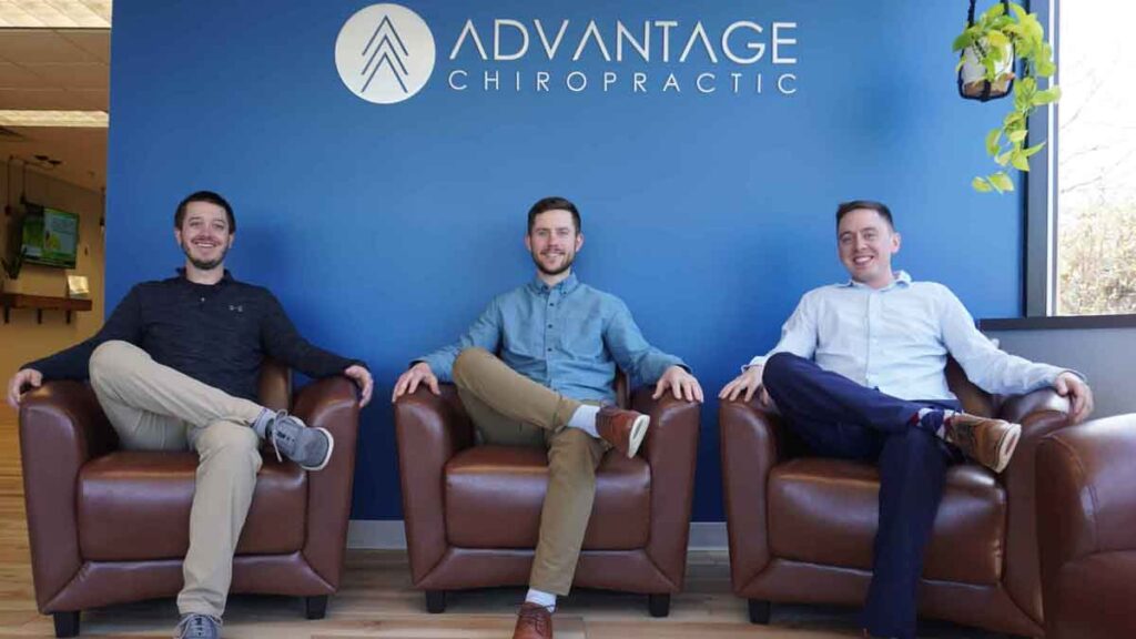 Advantage chiropractors sitting at the office posing for a picture in front of their logo on the wall.