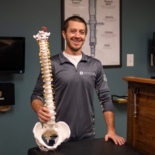 Chiropractor Dr. Zach Bruley of Advantage Chiropractic holding a model of a skeletal spine.