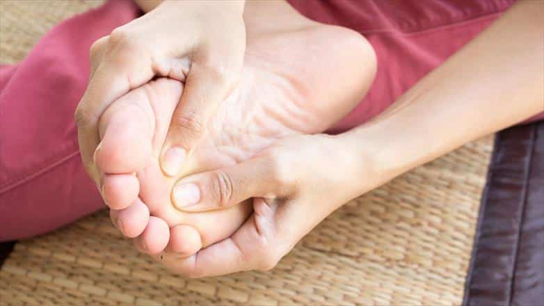 person with peripheral neuropathy symptoms holding foot.
