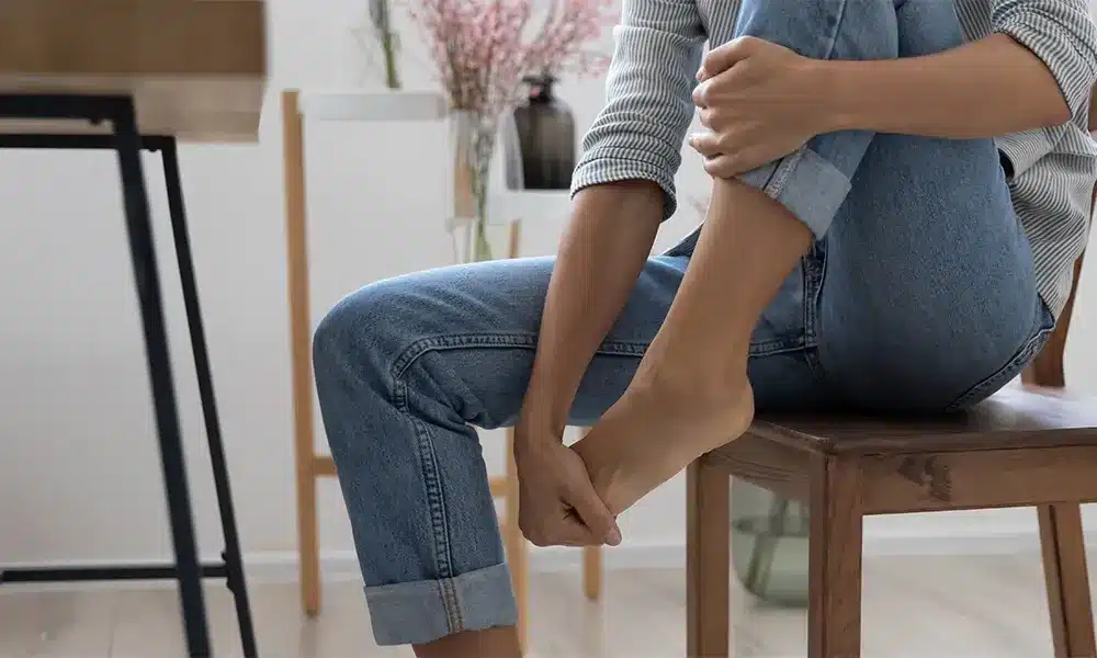 woman sitting in char with her leg raised holding her foot from neuropathy pain